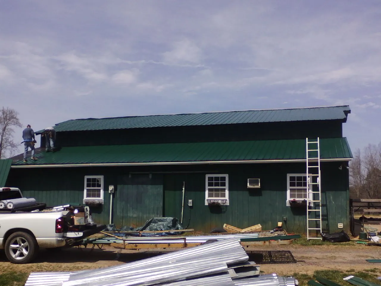 Crew installing green metal roofing on a large green barn in Boonville